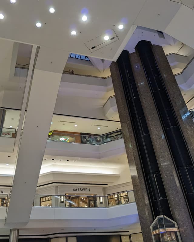The interior of a mall with multiple stories, an escalator, and elevators.