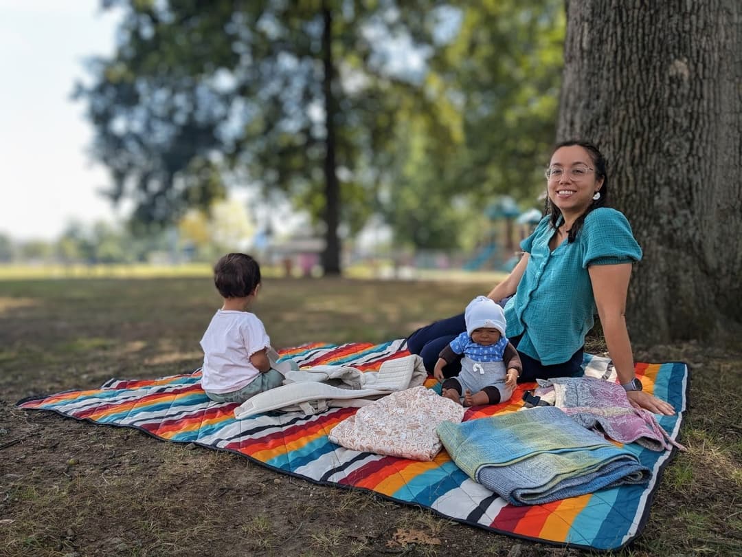 Waverly smiling on a forest path, wearing a soft-structured carrier with a child on her back.
