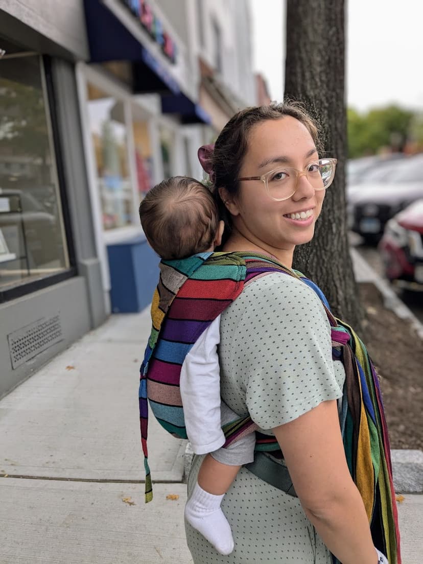 Waverly smiling, wearing a striped meh dai with a child on her back.