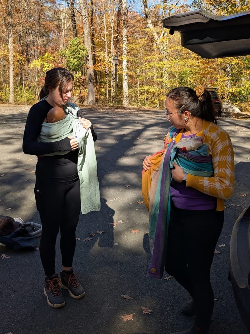 Waverly and another babywearing woman face each other, adjusting their ring slings and practice dolls.