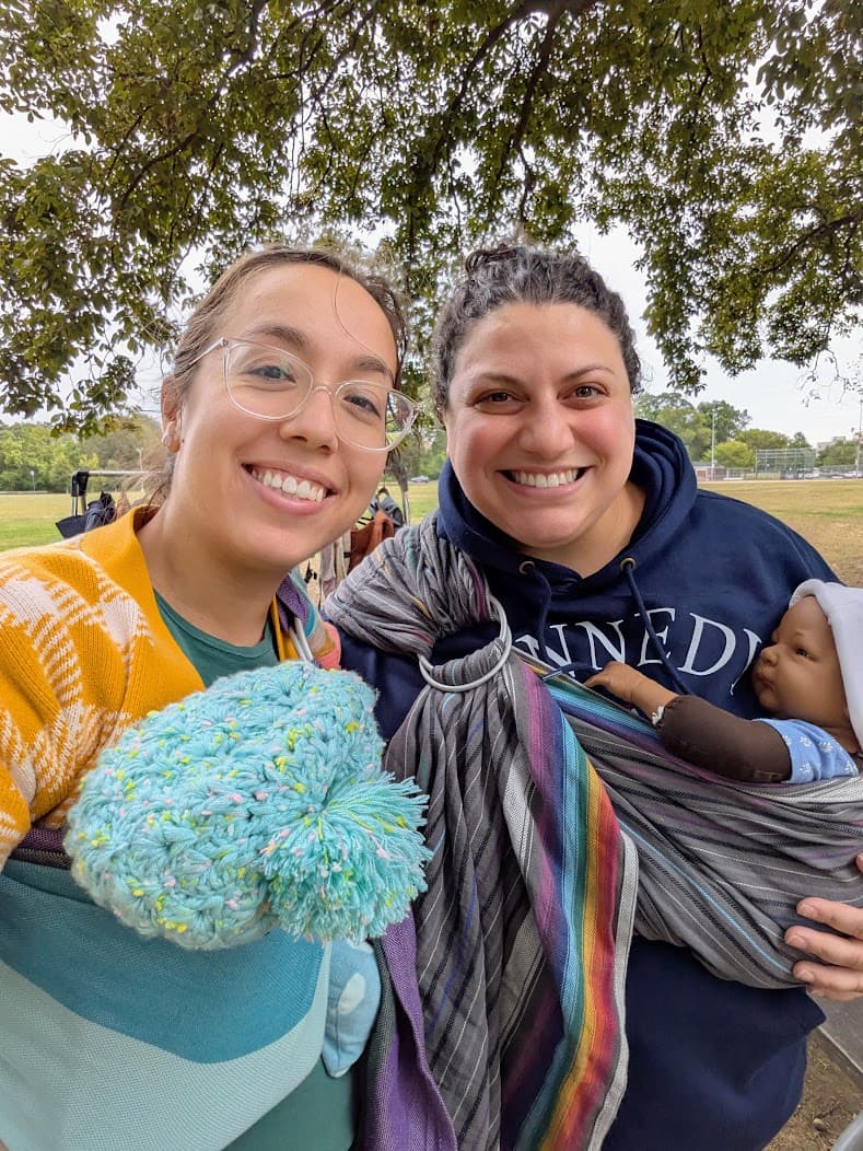 Waverly and another babywearing woman smiling, wearing ring slings and practice dolls.